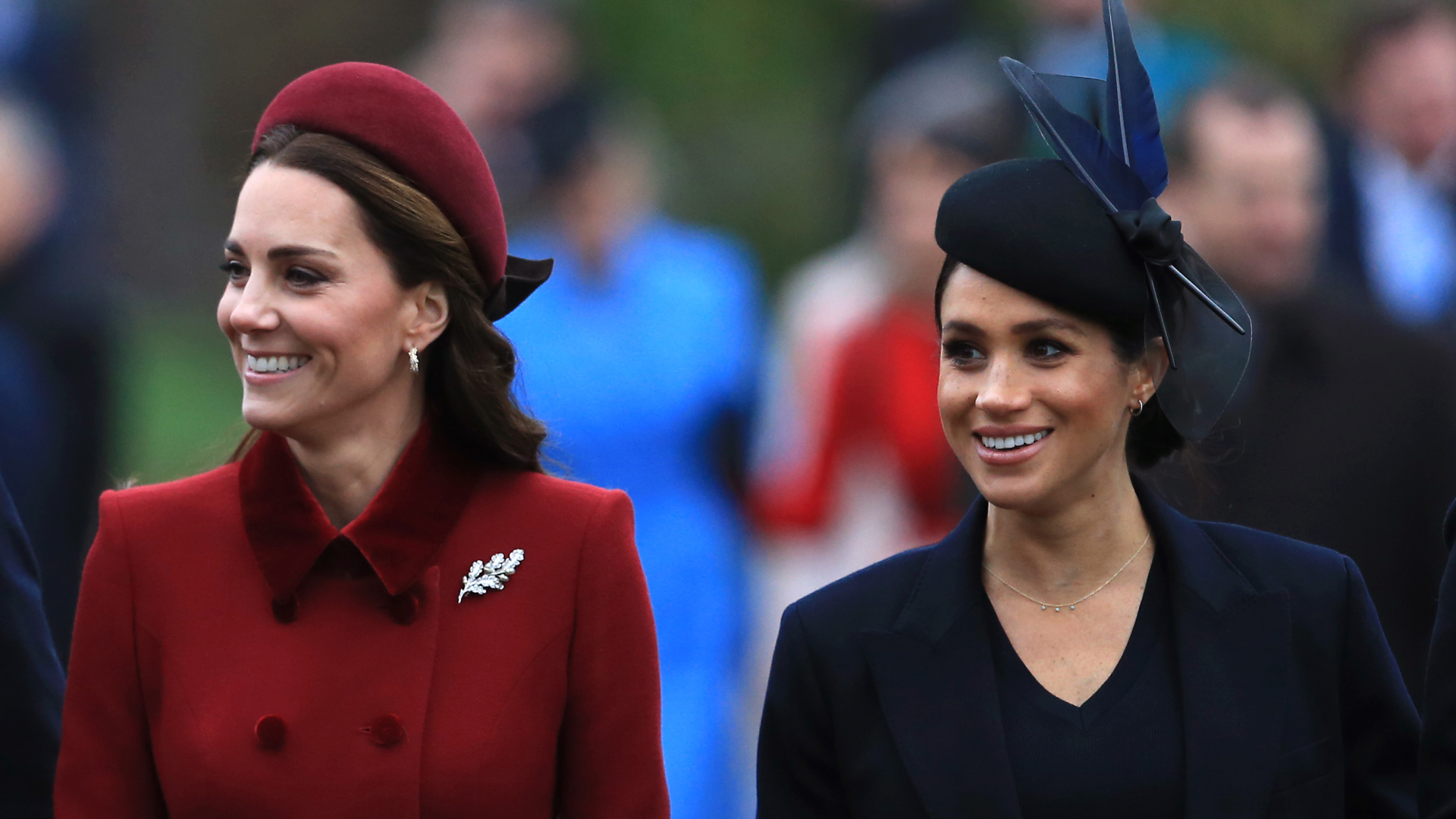Kate Middleton wears a dark red coat and matching hat while Meghan Markle wears a navy coat and matching hat
