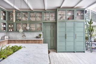 A large Shaker kitchen with pale green cabinets and raw wood base cabinets