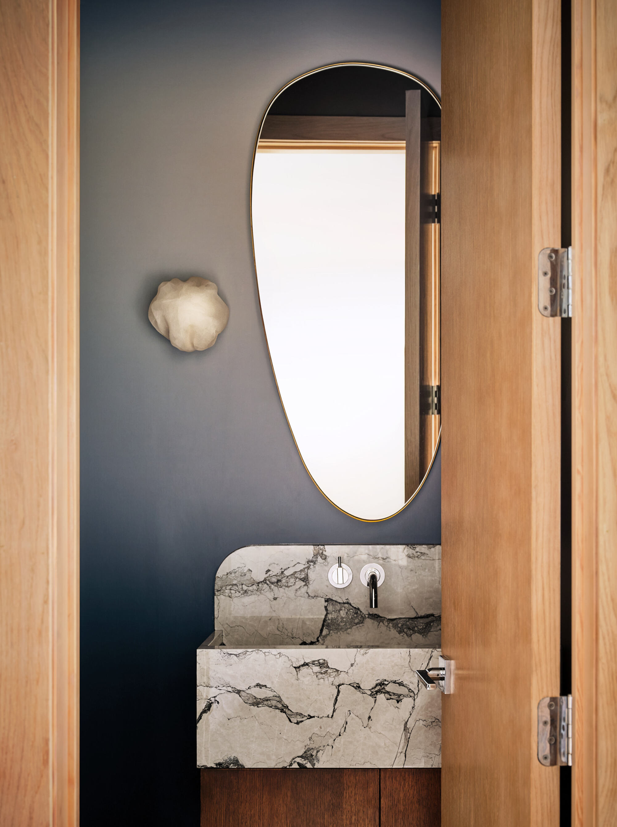 modern powder room with marble vanity, round mirror, statement wall sconce, and gradient wallcovering