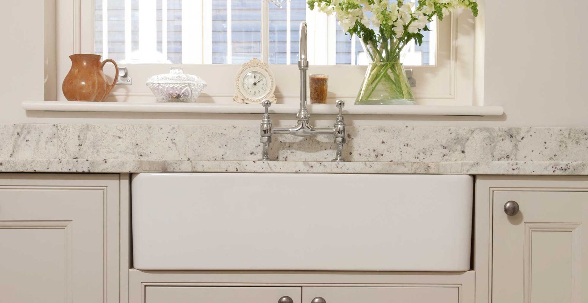A neutral kitchen with a ceramic butler sink in front of a window