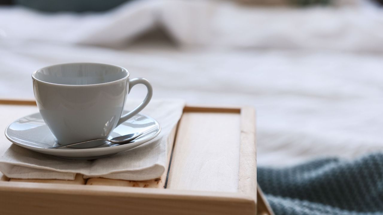 A cup of coffee on a wooden tray with a magazine, sitting on a bed