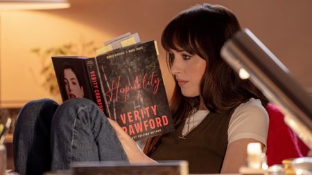 Dakota Johnson as Lowen reading a book with Anne Hathaway's Verity on the back cover. 