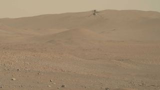 a small robotic helicopter hovers in front of a reddish-brown mountain on mars