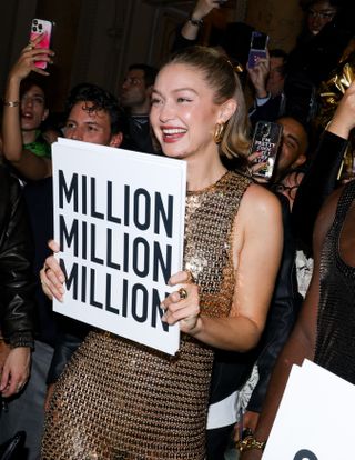 A closeup of Gigi Hadid holding a sign and sporting nude-colored nails.