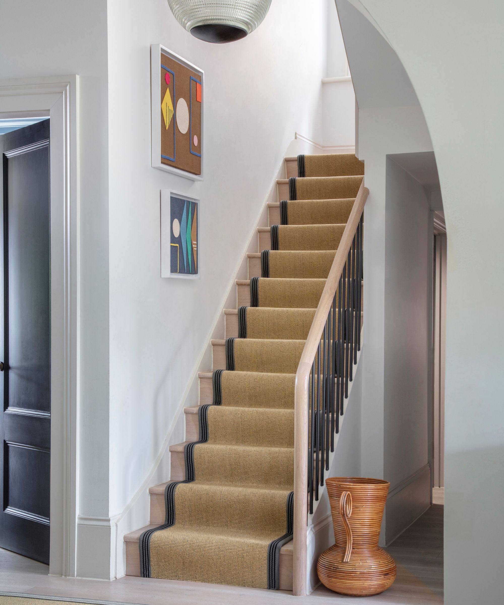 Bright staircase with neutral runner and subtle black edging, modern wall art and natural textures for a clean, inviting entrance.