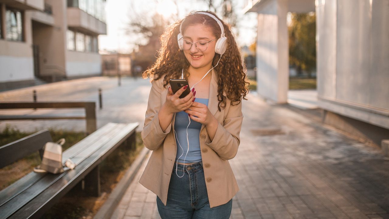 Woman walking wearing headphones and holding phone