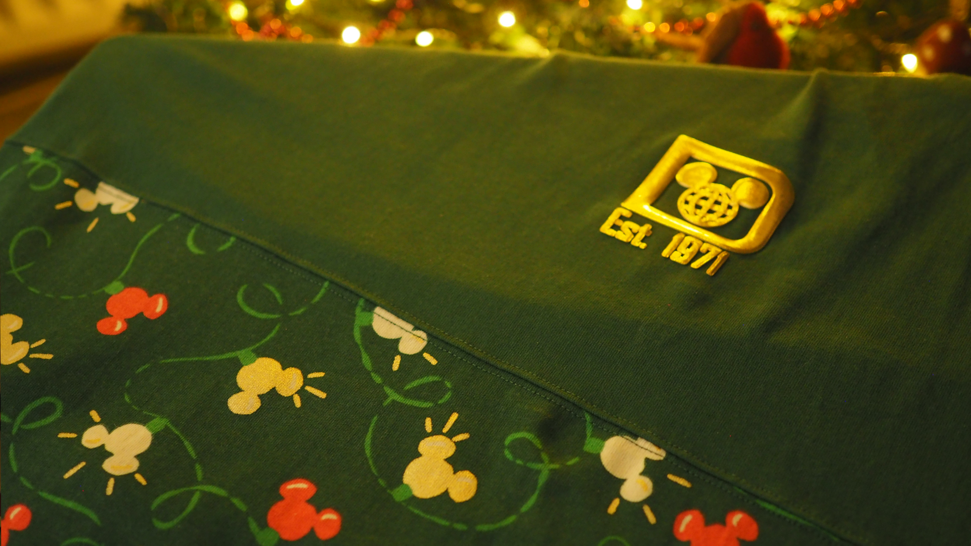 Green Disney Christmas sweater with a Disney World logo in embossed gold, a bauble pattern, and a tree in the background