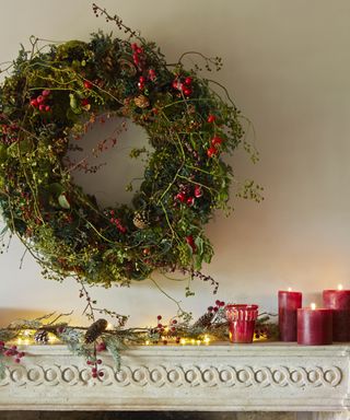 Christmas wall decor ideas with a large wreath over a mantel decorated with red candles