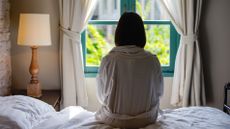 Woman sat on bed looking out window 