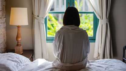 Woman sat on bed looking out window 