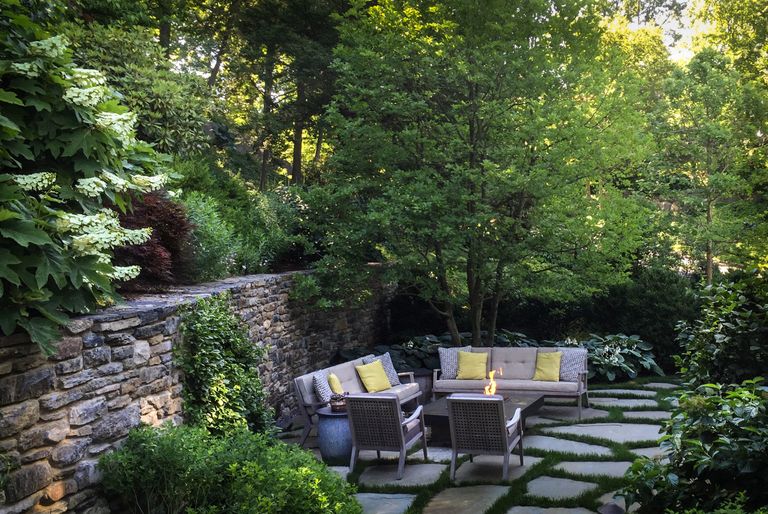 stone garden wall enclosing a seating area and patio with lush green planting all around