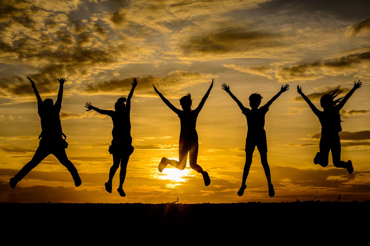 Five people jumping on a beach at sunset