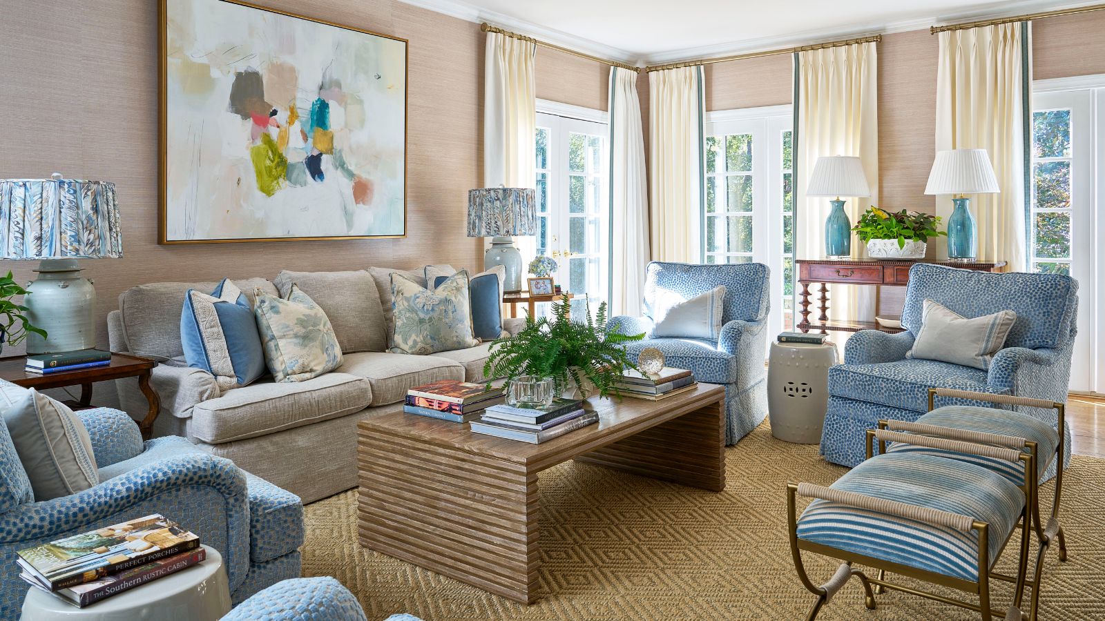Living room with pale pink grasscloth walls, wooden coffee table, blue and cream sofas and armchairs and mahogany tables with large lamps