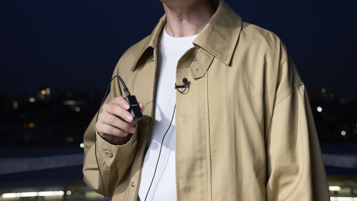 Sony ECM-L1 microphone clipped to a person&#039;s jacket with the receiver held in a hand