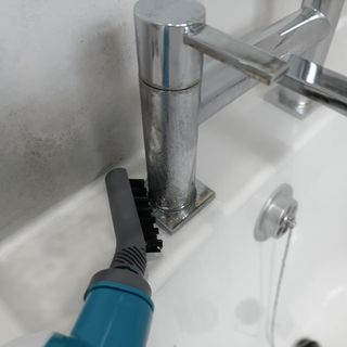 Closeup of a small steam cleaner tool head being used to clean a metallic bath tap.
