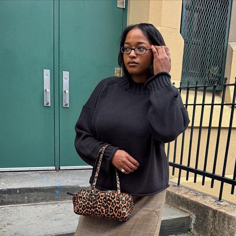 a woman wearing a black sweater, plaid skirt, and black boots