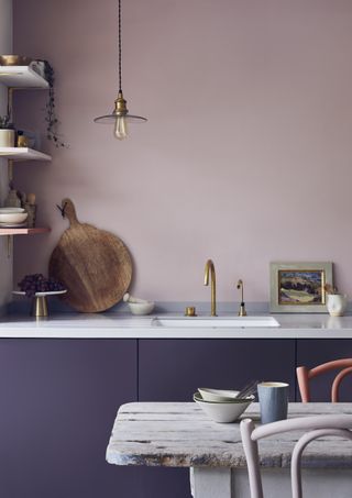 kitchen with dark purple cabinets, blush pink wall, white countertop, open shelving, brass fixtures, rustic table