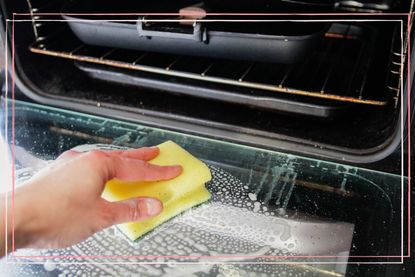 A close up of a soapy sponge cleaning an oven door