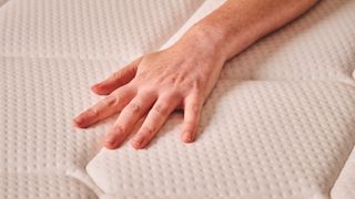 A hand presses into the surface of the Plank Firm mattress, testing the temperature regulation, pressure relief, and firmness