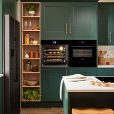 Green kitchen with fitted oven in cabinetry, stainless steel fridge and hob on island