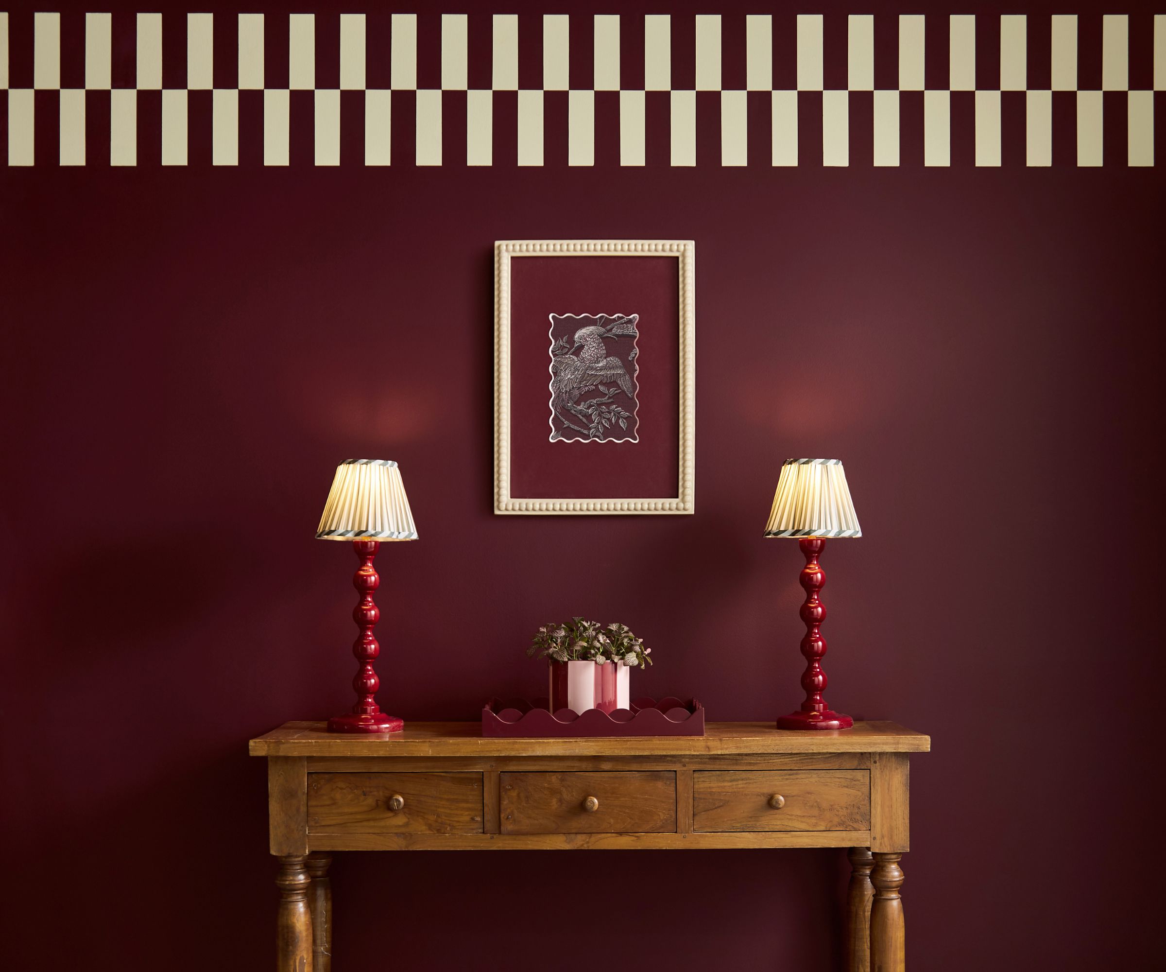 Burgundy painted wall in an entryway with checkerboard ceiling trim and a wooden console with two red table lamps