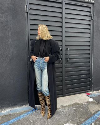 Elsa Hosk wearing a black coat, jeans, and leopard-print boots.