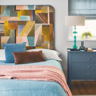 how to make a guest room look more expensive, modern bedroom with white walls blue side table, blue and pink throws, bold abstract upholstered headboard, wooden floor