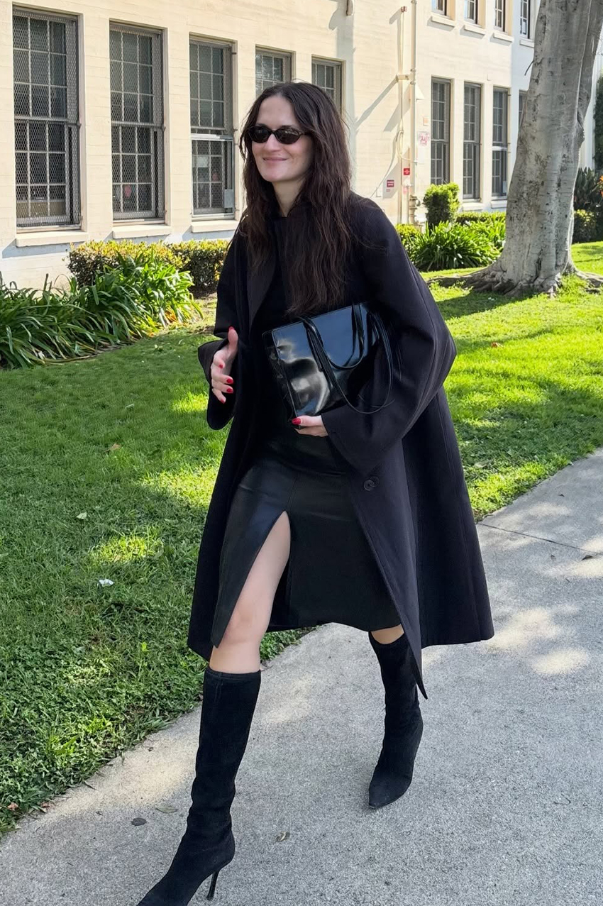 a woman wearing a black coat, black skirt, and black knee high boots