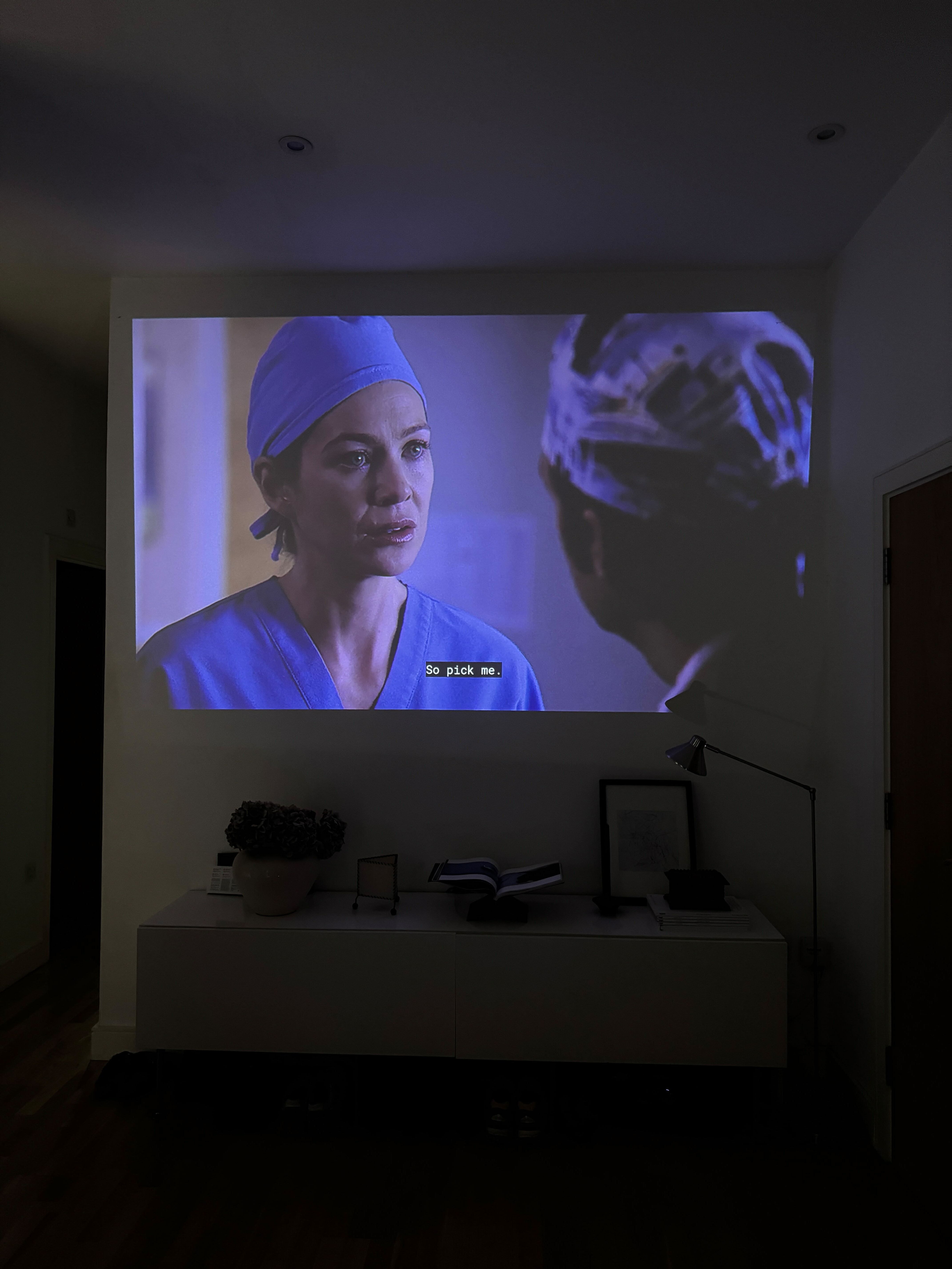 scene from grey&#039;s anatomy with meredith grey projected onto a wall with the subtitles &quot;pick me&quot;