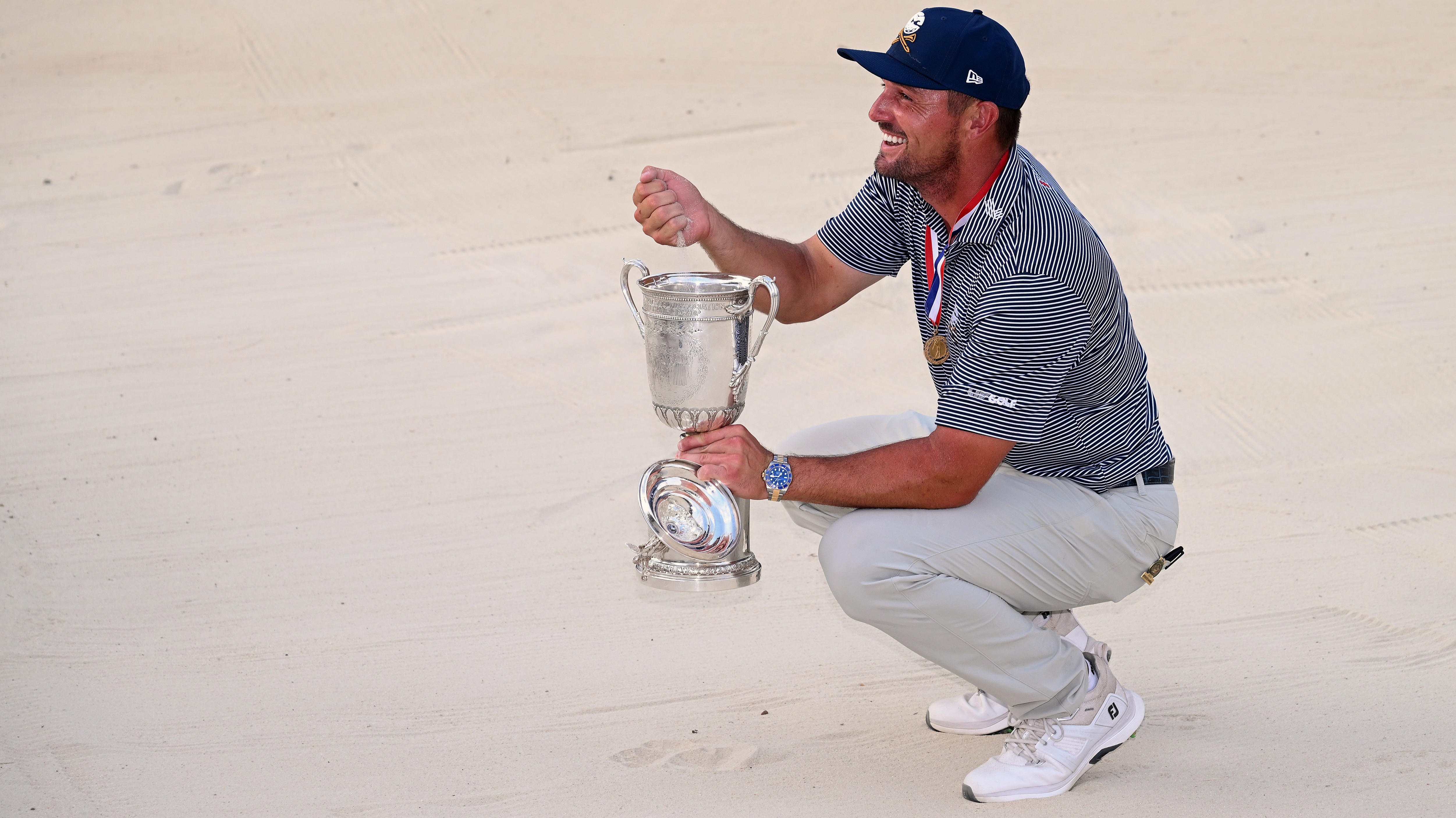 Bryson DeChambeau celebrates with the trophy in the bunker where he played his superb third shot on the 18th hole during the final round of the 124th U.S. Open at Pinehurst 