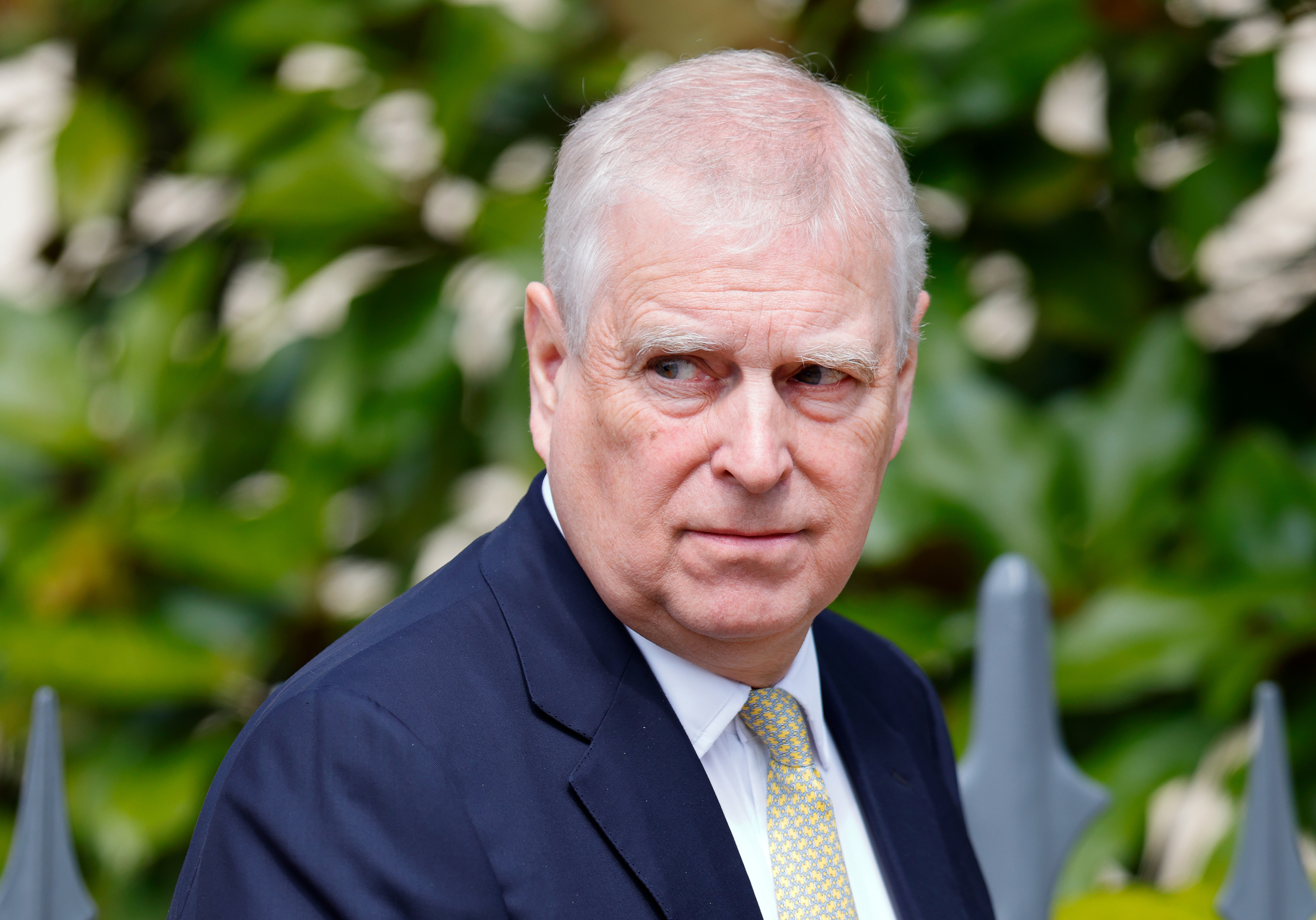 Prince Andrew wearing a navy suit walking in front of bushes
