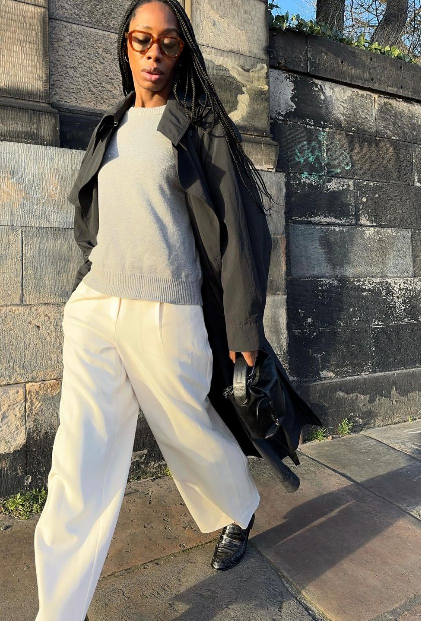 @louisahatt wears a grey knit jumper, black trench coat, white trousers and black loafers