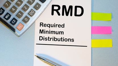The words RMD and required minimum distributions are typed on a notecard next to a calculator and pen.