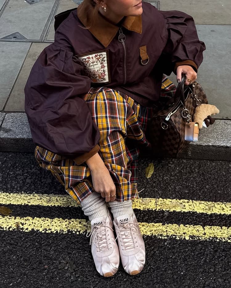 An image of @rebeccaferrazwyatt wearing a pair of pink satin trainers from Miu Miu with a plaid skirt and a jacket from Farm Rio x Barbour.