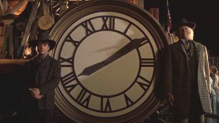 Michael J Fox and Christopher Lloyd pose for a photo in front of a clock face in Back To The Future: Part III.