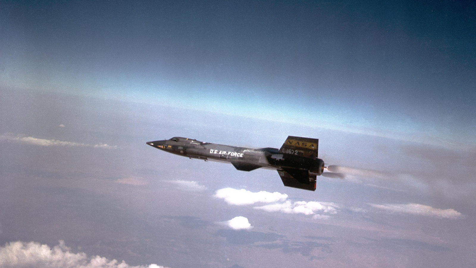 A dark colored plane glides above the clouds