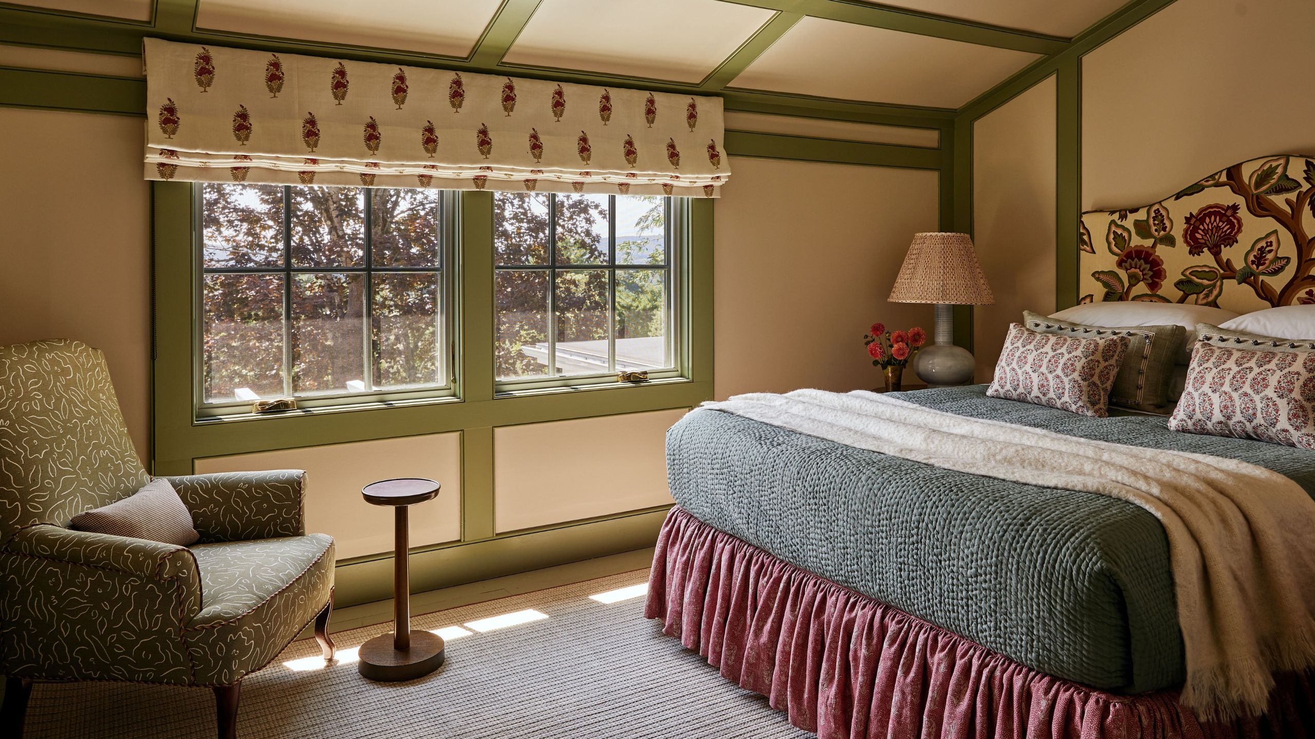 a bright, warm guest bedroom with green painted wall molding trim, floral headboard, bedskirt and layered linens