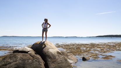 Mature woman on a rock looking out at the water in Maine.