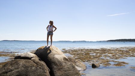 Mature woman on a rock looking out at the water in Maine.