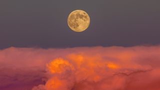 Full moon above orange and pink hued storm clouds