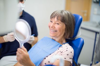 A woman sits in a dentist's chair smiling into a mirror. 