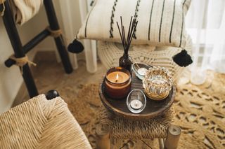 Home decor with burning candles and a black reed diffuser on a wooden coffee table in a cosy living room.