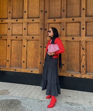 Yusra Siddiqui during NYFW wearing a red sweater with a black skirt and red tights.