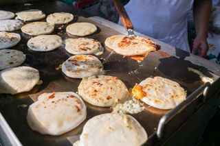 A man griddles several pupusas on an outdoor grill in El Salvador