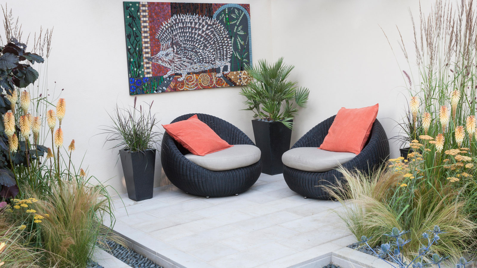 small patio with planting around it, two lounge chairs, planters and wall art of hedgehog
