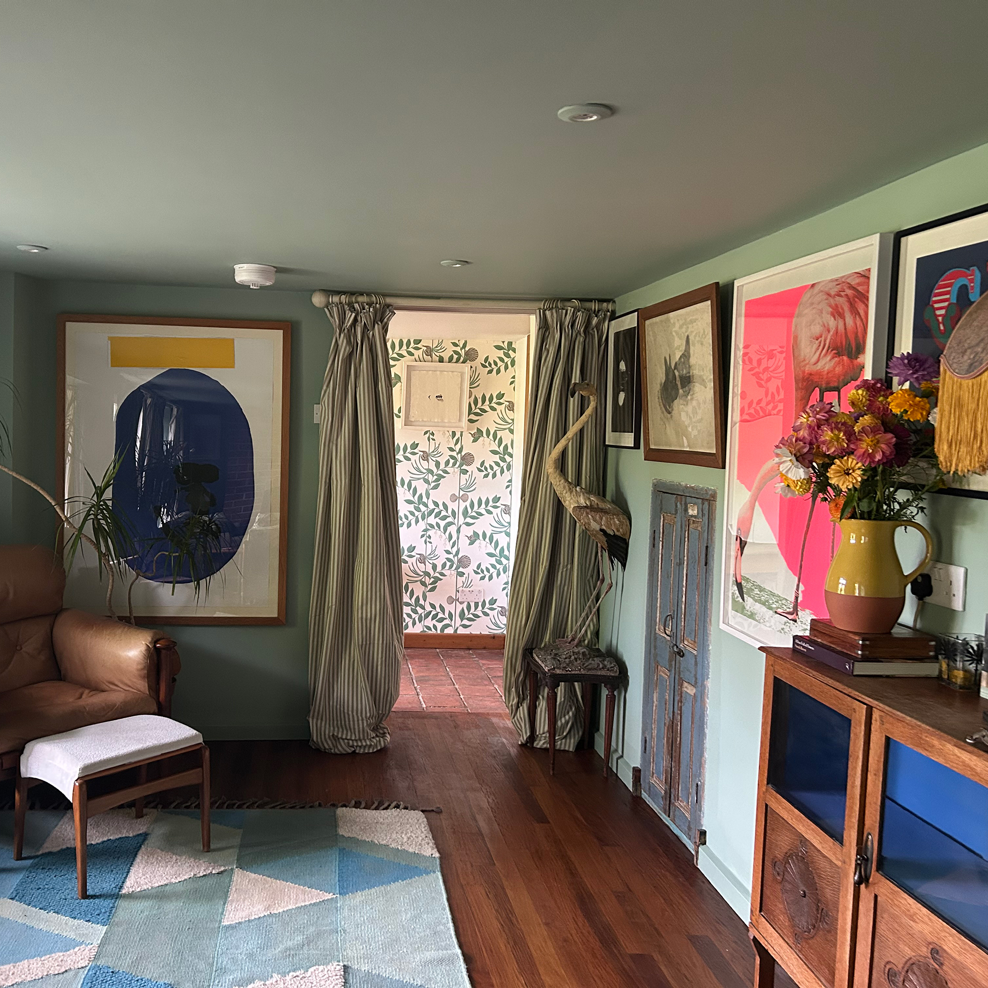 Green room with wooden floor and blue and green patterned rug, framed artworks on wall