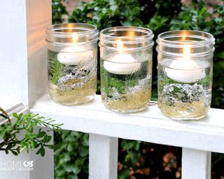 A trio of homemade candles in mason jars with pine decor, tea lights and gel
