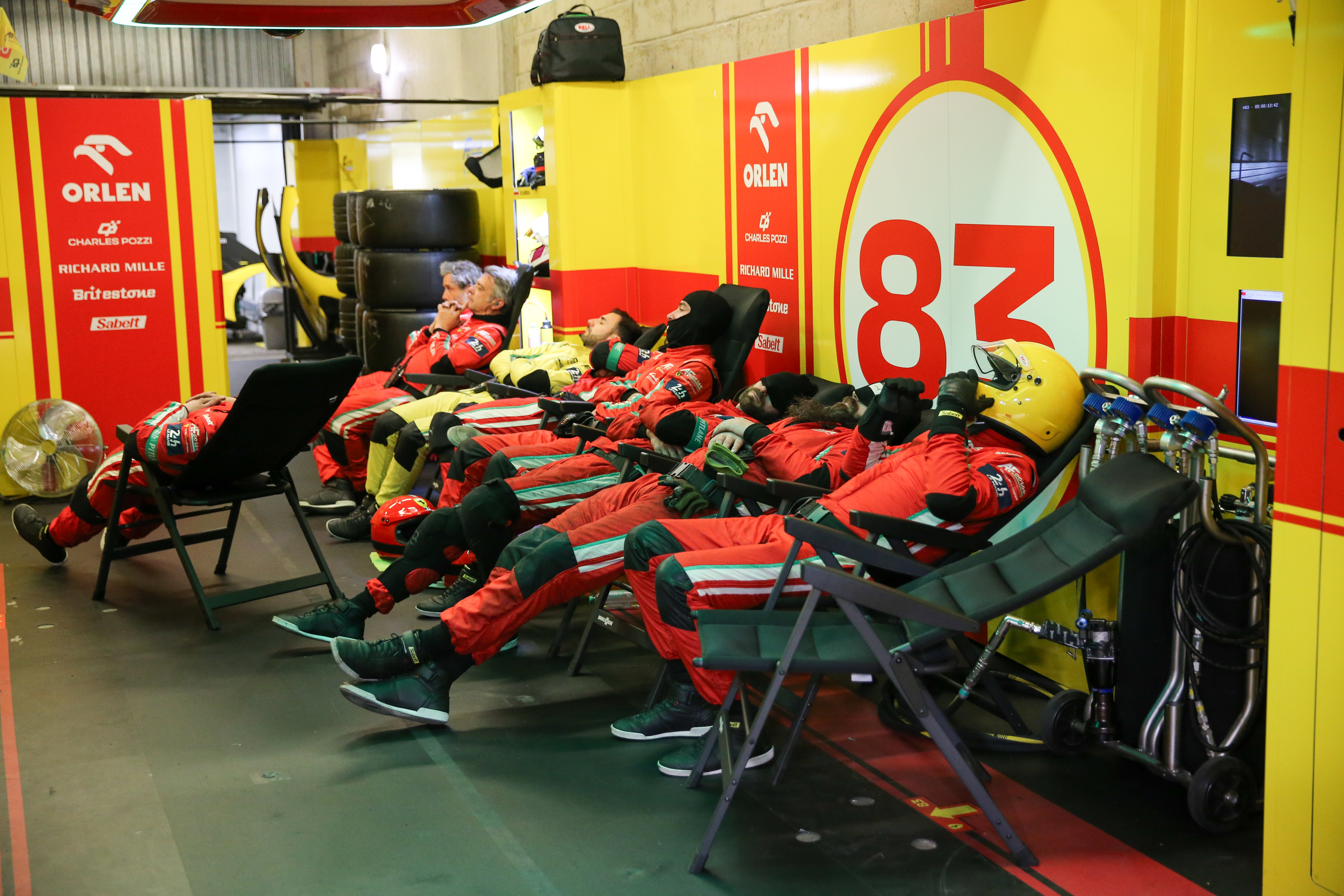 Mechanics in red overalls taking a nap at Le Mans 2025