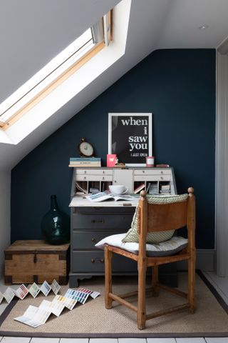 Pippa Jones house: home office corner with dark blue wall under sloping rooflight, dark blue painted bureau, wood chair and 'When I saw you' monochrome print