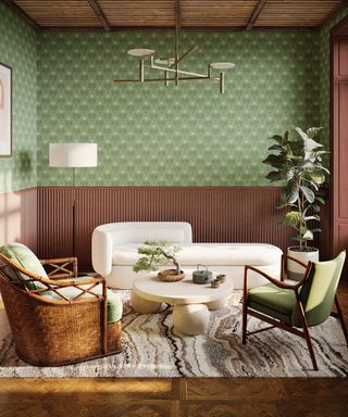 A living room with green wallpaper with brown paneling, a white couch, a woven chair, a green chair and a wooden floor with a woven rug on it